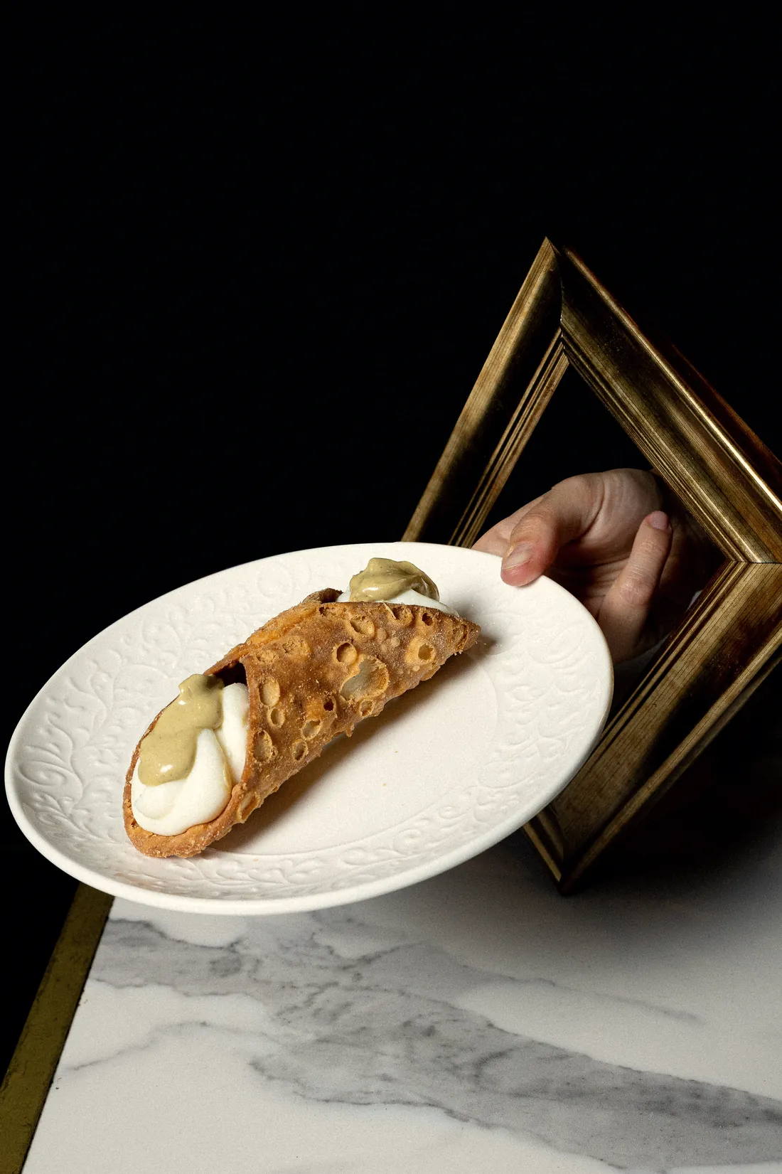 Cannolo siciliano su un piatto bianco con una cornice dorata