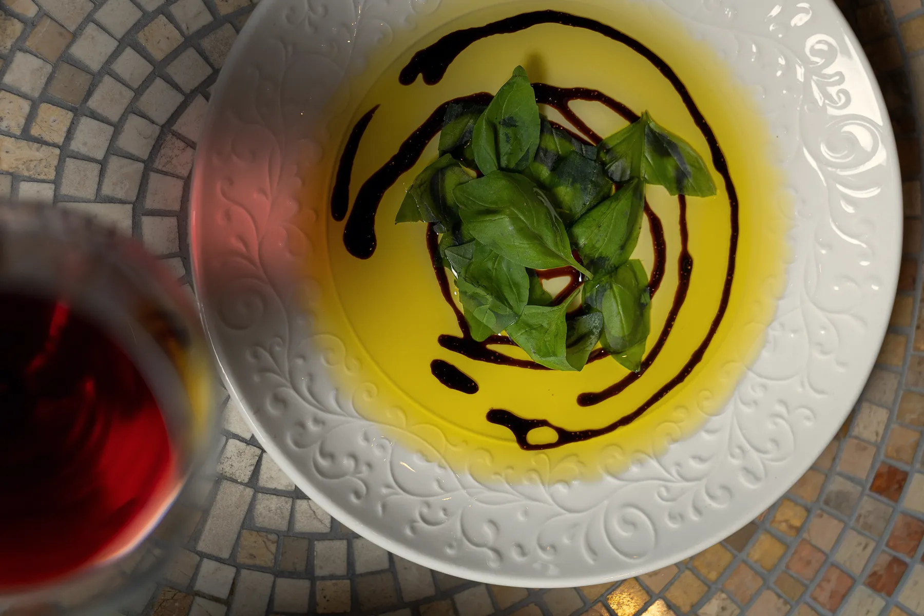 Piatto con basilico e riduzione, vino rosso sullo sfondo
